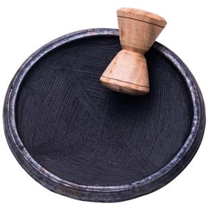 May include: A black mortar and pestle set. The mortar is round with a dark interior and a silver rim. The pestle is made of light-colored wood. The mortar's interior has a textured surface.