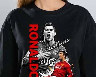 May include: Black t-shirt featuring a graphic of Cristiano Ronaldo in a red soccer jersey, with the name "RONALDO" in red vertical text. The image includes the word "cristiano" in cursive.