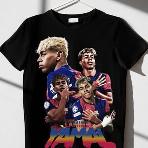 May include: Black t-shirt with a graphic of a soccer player in a red and blue kit. The shirt displays the name "LAMINE YAMAL" in colourful text. The design incorporates multiple images of the player.
