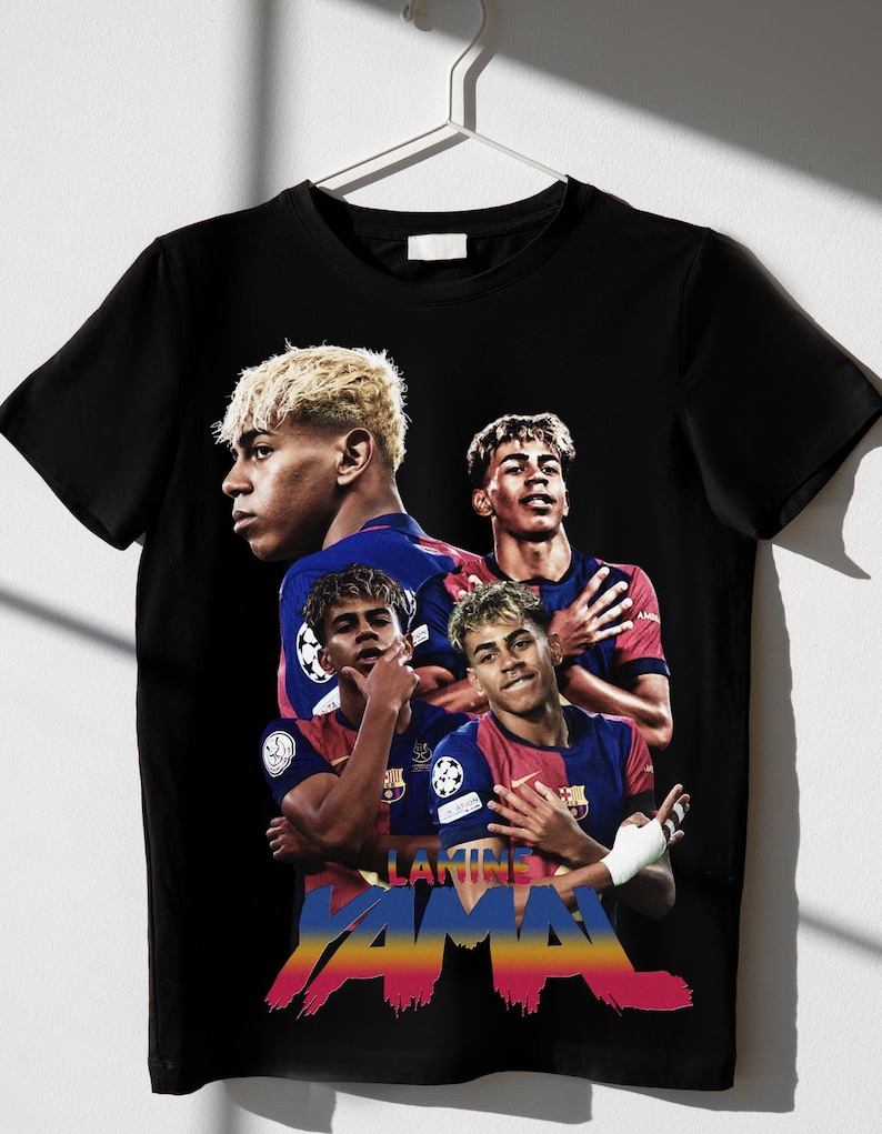 May include: Black t-shirt with a graphic of a soccer player in a red and blue kit. The shirt displays the name "LAMINE YAMAL" in colourful text. The design incorporates multiple images of the player.