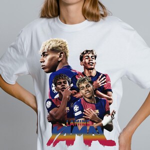 May include: White t-shirt with a graphic of a footballer in a blue and red kit. The design includes the name "Lamine Yamal" in colourful text. The graphic features multiple images of the player in action.