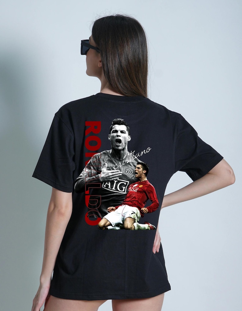 Pu&ograve; includere: T-shirt nero con grafica di un calciatore in maglia rossa, con il nome "Ronaldo" in testo verticale rosso. La maglietta include anche il testo "Cristiano".