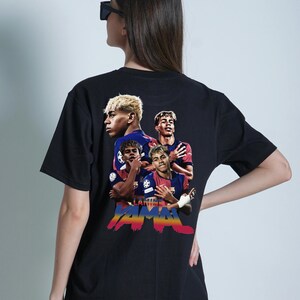 May include: Black t-shirt with a vibrant graphic of soccer players. The design incorporates the text "Lamine Yamal" in a colourful, stylized font. The shirt has a crew neck and short sleeves.