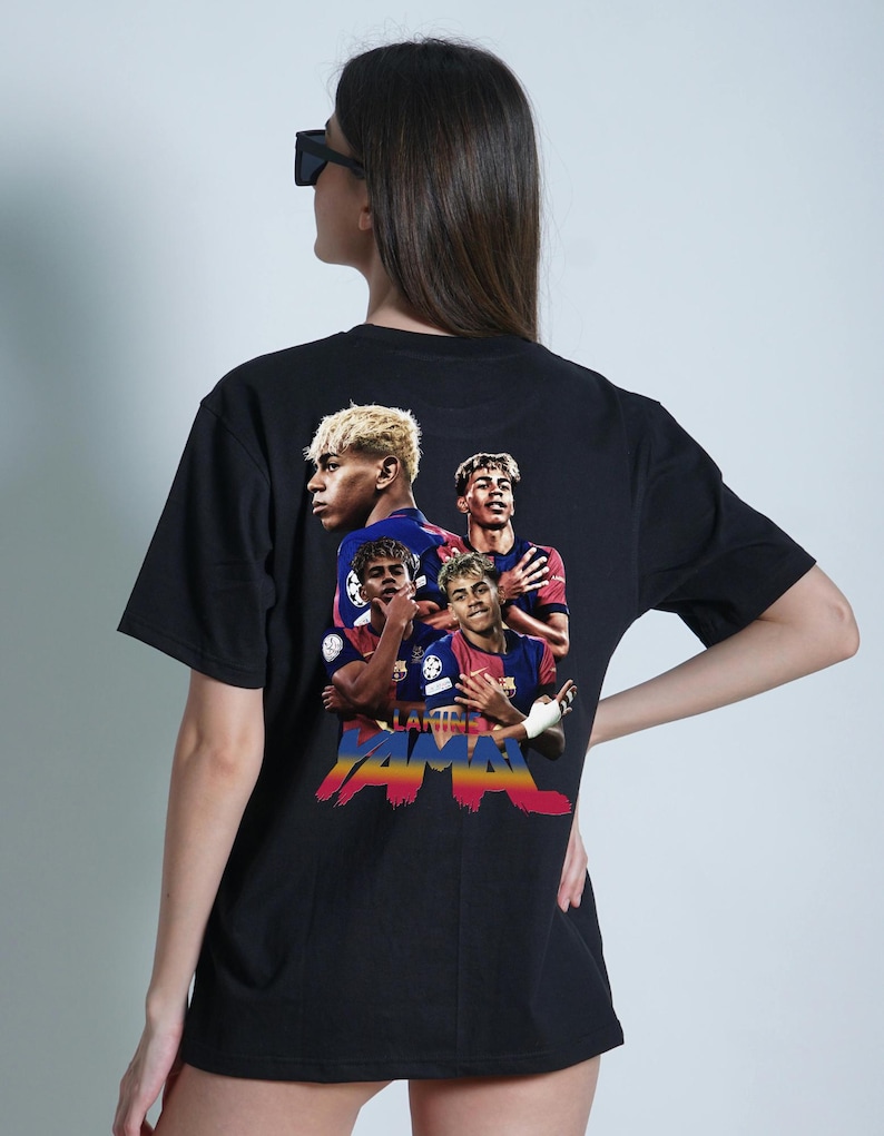 May include: Black t-shirt with a vibrant graphic of soccer players. The design incorporates the text "Lamine Yamal" in a colourful, stylized font. The shirt has a crew neck and short sleeves.