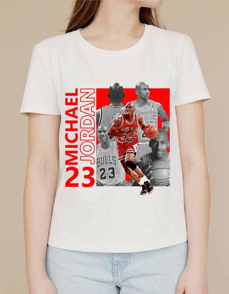 May include: White t-shirt featuring a collage of Michael Jordan images in red and grayscale. The design includes the text "MICHAEL JORDAN 23" in red vertical lettering. The images show Jordan in his Bulls uniform.