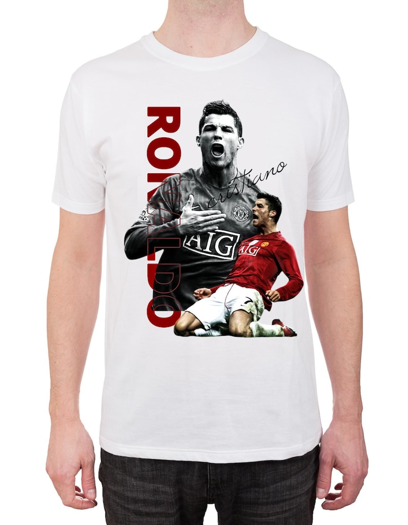 Pu&ograve; includere: T-shirt bianco con grafica di un calciatore in maglia rossa, con la scritta "RONALDO" in rosso in verticale. La maglietta include anche una firma e i loghi "AIG" e "Nike".
