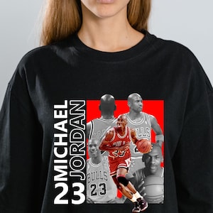 May include: Black t-shirt featuring a graphic of Michael Jordan in a red and white Bulls uniform, holding a basketball. The design includes the text "MICHAEL JORDAN 23" in white, with additional images of Jordan in the background.