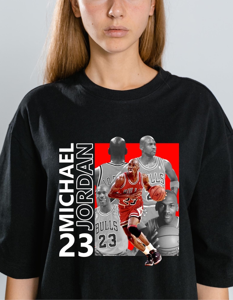 May include: Black t-shirt featuring a graphic of Michael Jordan in a red and white Bulls uniform, holding a basketball. The design includes the text "MICHAEL JORDAN 23" in white, with additional images of Jordan in the background.