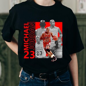 May include: Black t-shirt featuring a graphic of Michael Jordan in a red and white Chicago Bulls uniform, with the text "MICHAEL JORDAN 23" in red. The design includes multiple images of Jordan.
