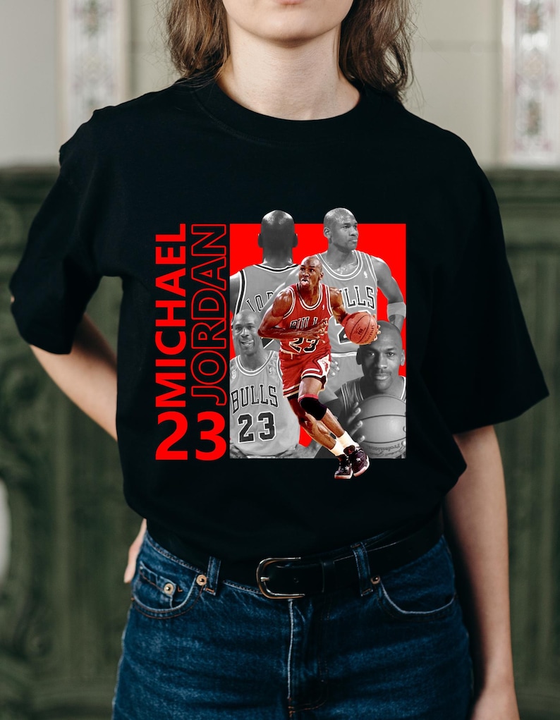May include: Black t-shirt featuring a graphic of Michael Jordan in a red and white Chicago Bulls uniform, with the text "MICHAEL JORDAN 23" in red. The design includes multiple images of Jordan.