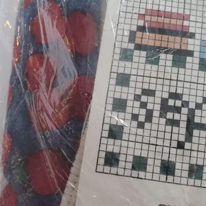 May include: A cross-stitch kit in a clear plastic package. The kit includes a piece of fabric with a printed grid, colorful embroidery floss, and a pattern chart. The pattern appears to be a pixelated design. The fabric has a blue background with red circles.