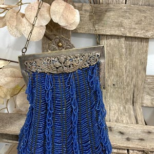 May include: Vintage blue beaded handbag with a silver-tone frame and chain strap. The bag features intricate beadwork and a decorative floral clasp. The beaded fringe adds a touch of elegance to this classic accessory.