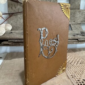 May include: A vintage brown book with the word "Poest" in silver script. The book has gold corner accents. The cover is a textured brown material, and the book appears to be old.