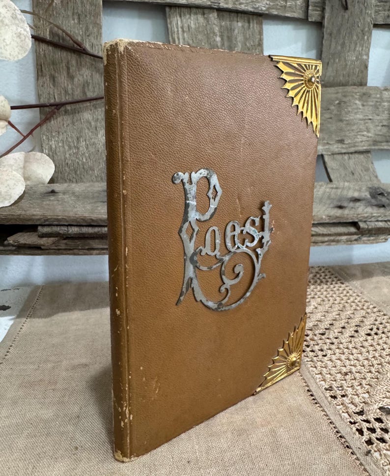 May include: A vintage brown book with the word "Poest" in silver script. The book has gold corner accents. The cover is a textured brown material, and the book appears to be old.