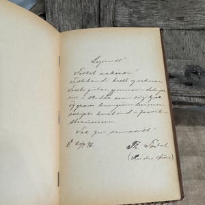 May include: Open vintage book with handwritten text in black ink on aged, cream-colored pages. The book is bound with a brown cover and is open to a page with cursive writing and signatures.