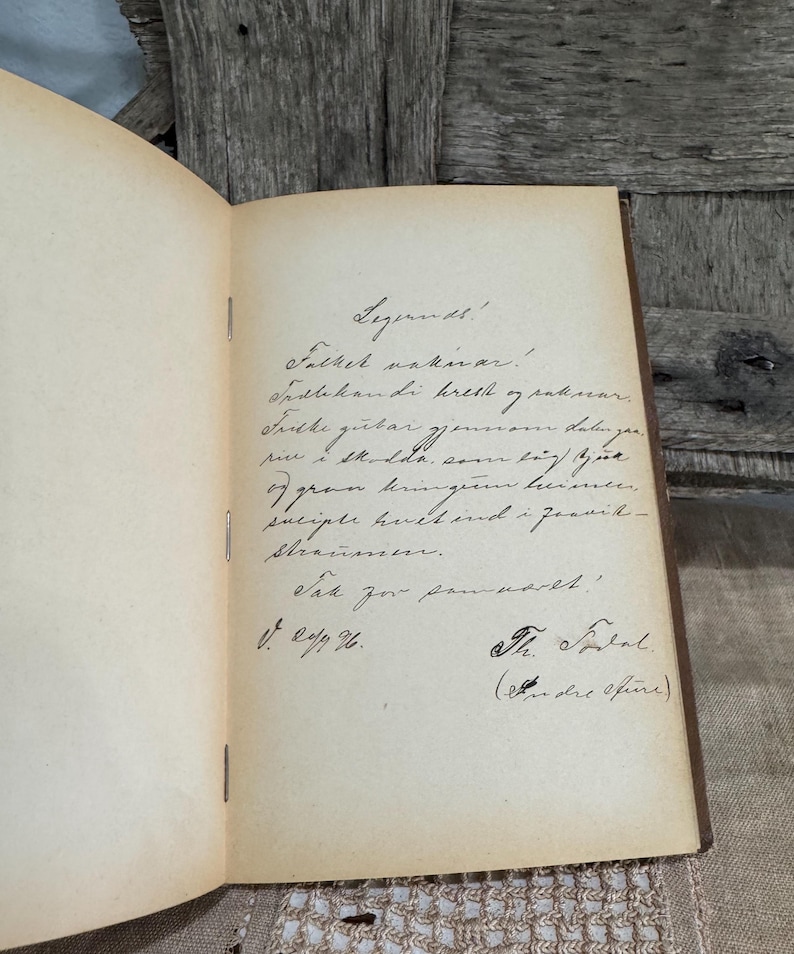 May include: Open vintage book with handwritten text in black ink on aged, cream-colored pages. The book is bound with a brown cover and is open to a page with cursive writing and signatures.