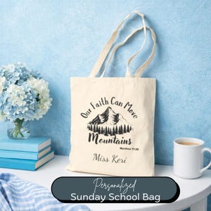 May include: Cream-colored tote bag with the text "Our Faith Can Move Mountains" and a mountain graphic. The bag includes the name "Miss Keri" and the text "Matthew 17:20". The words "Personalized Sunday School Bag" are at the bottom.