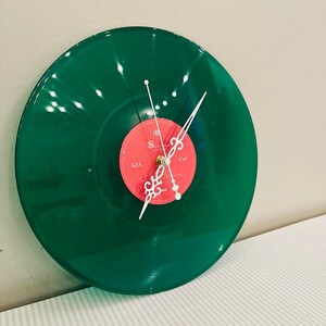 May include: A green vinyl record clock with white clock hands and a red center label. The clock hands are white and the center label has the text "SZA" and "Ctrl". The clock is mounted on a white wall.