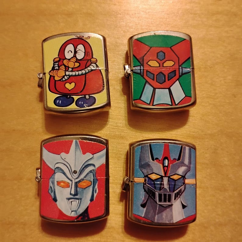 Puede incluir: Cuatro encendedores met&aacute;licos vintage con coloridos dise&ntilde;os de dibujos animados y robots. Los encendedores presentan un personaje de dibujos animados rojo, un robot con detalles en verde y rojo, un robot con fondo rojo y un robot con fondo azul.