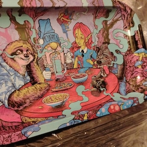 May include: A colorful metal rolling tray featuring a whimsical illustration. The tray depicts a sloth, a gnome, and other fantasy creatures gathered around a red table. The artwork is set against a backdrop of trees and mushrooms.