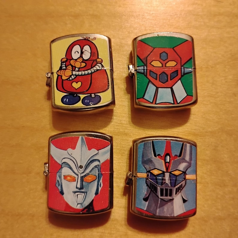 Puede incluir: Cuatro encendedores met&aacute;licos vintage con dise&ntilde;os de dibujos animados coloridos. Los encendedores presentan varios personajes en rojo, amarillo, azul y verde. Los encendedores est&aacute;n dispuestos en un cuadrado sobre una superficie de madera.