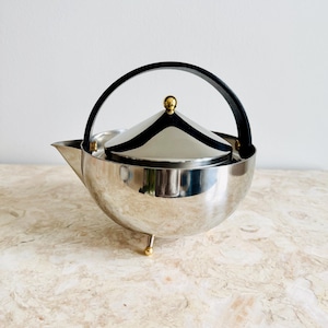 Könnte beinhalten: Ein Set aus drei Keramikbechern mit gesprenkelter, matter Oberfläche. Die Becher sind in den Farbtönen Creme, Hellgrau und Dunkelgrau gehalten. Jeder Becher hat ein schlichtes, minimalistisches Design und einen abgerundeten Henkel.