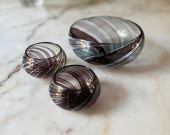 Könnte beinhalten: Drei Glasschalen mit einem wirbelnden Muster aus Lila, Weiß und Blau. Die Schalen sind ineinander verschachtelt, wobei die größte Schale unten und die kleinste Schale oben liegt.