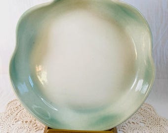 May include: A ceramic serving plate with a scalloped edge. The plate has a white center with a soft green and beige gradient around the rim. It is displayed on a gold-colored stand, showcasing its elegant design.