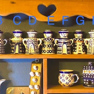 May include: A wooden shelf displays a collection of Polish pottery figurines, each with a unique design in blue, white, and yellow. Below, a teapot, mug, and other pottery pieces complement the display. The shelf has a heart-shaped cutout.