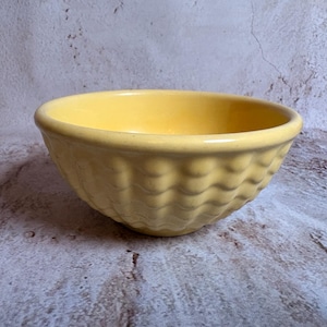 May include: A yellow ceramic bowl with a wavy, textured exterior. The bowl has a rounded shape and a smooth, glossy interior. The bowl is likely used for serving food or as a decorative item.