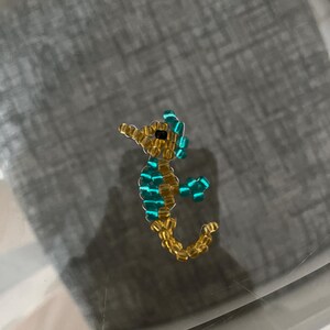 Pu&ograve; includere: Una statuetta di cavalluccio marino di perline. Il cavalluccio marino &egrave; realizzato con piccole perline dorate per il corpo e la testa, e perline turchesi per le pinne e gli accenti. &Egrave; un piccolo oggetto decorativo.