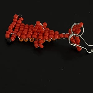 Pu&ograve; includere: Un portachiavi fatto a mano con perline rosse a forma di dinosauro. Il dinosauro &egrave; realizzato con piccole perline rosse rotonde, infilate con filo d'argento. Il portachiavi ha un portachiavi argentato.