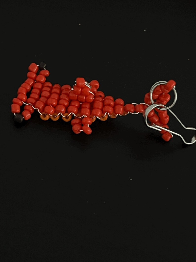Pu&ograve; includere: Un portachiavi fatto a mano con perline rosse a forma di dinosauro. Il dinosauro &egrave; realizzato con piccole perline rosse rotonde, infilate con filo d'argento. Il portachiavi ha un portachiavi argentato.