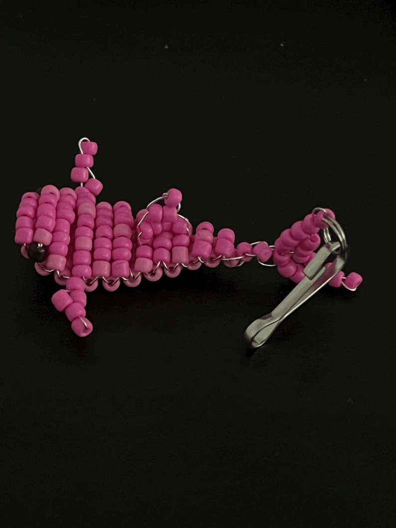 Pu&ograve; includere: Un portachiavi rosa a perline a forma di pesce. Il pesce &egrave; fatto di piccole perline rosa rotonde infilate con filo d'argento. Un fermaglio color argento &egrave; attaccato alla coda del pesce.