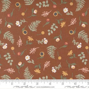 May include: Brown fabric with a repeating floral pattern. The design includes white daisies, yellow sunflowers, and green fern leaves. The fabric also features small pink and yellow buds and light pink leaf sprigs. The bottom of the image shows a ruler.