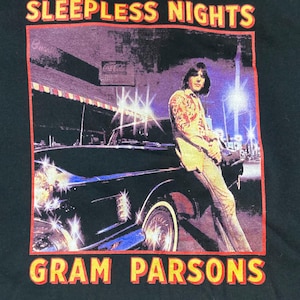 May include: Black t-shirt featuring a vintage image with the text "SLEEPLESS NIGHTS" and "GRAM PARSONS" in yellow and red. The image depicts a person leaning against a car at night.