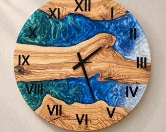 Puede incluir: Un reloj de pared redondo con una esfera de madera natural que presenta dos secciones de resina azul y turquesa con efecto remolino. El reloj tiene números romanos negros del I al XII y manecillas negras finas en el centro de la esfera.