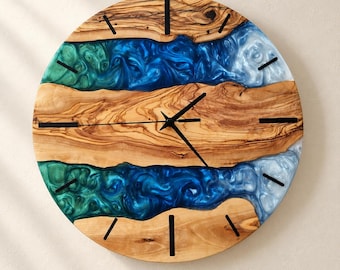 Puede incluir: Un reloj de pared redondo con secciones de madera natural de color marrón claro separadas por dos bandas horizontales de resina con remolinos azules, turquesas y blancos. La esfera incluye marcadores de hora y manecillas negras.