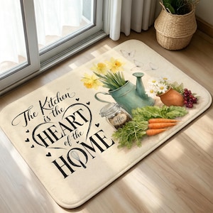 Könnte beinhalten: Eine rechteckige Bodenmatte mit dem schwarzen Text The Kitchen is the HEART of the HOME und einem Schneebesen-Symbol. Das Design zeigt eine türkisfarbene Gießkanne mit gelben Narzissen, ein Glas mit der Aufschrift coffee, Karotten und weiße Blumen.