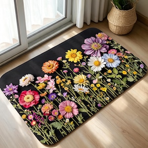 May include: A rectangular floor mat with a black background featuring a vibrant, colorful print of various wildflowers including daisies, zinnias, and cosmos in shades of pink, purple, yellow, orange, and white, with green stems and leaves.