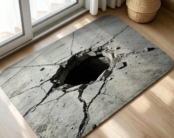 May include: A rectangular floor mat featuring a high-resolution print of a cracked concrete surface with a large, dark, central hole. The design mimics a broken pavement texture in shades of gray, with jagged fissures radiating outward.