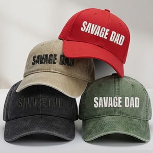 May include: Four baseball caps in red, tan, black, and green. Each cap has the text "SAVAGE DAD" in white block letters. The caps are arranged in a stack, with the red cap on top. The text "MIUCUNSTORE PERSONALIZED GIFTS" is at the top.