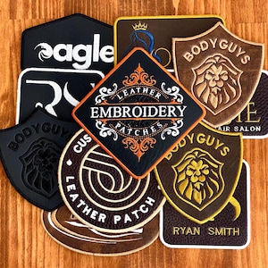 May include: A collection of embroidered leather patches in various shapes and colors. The patches feature text such as "Eagle", "Body Guys", and "Leather Embroidery Patches". Some patches have logos, including a lion's head and a crown.