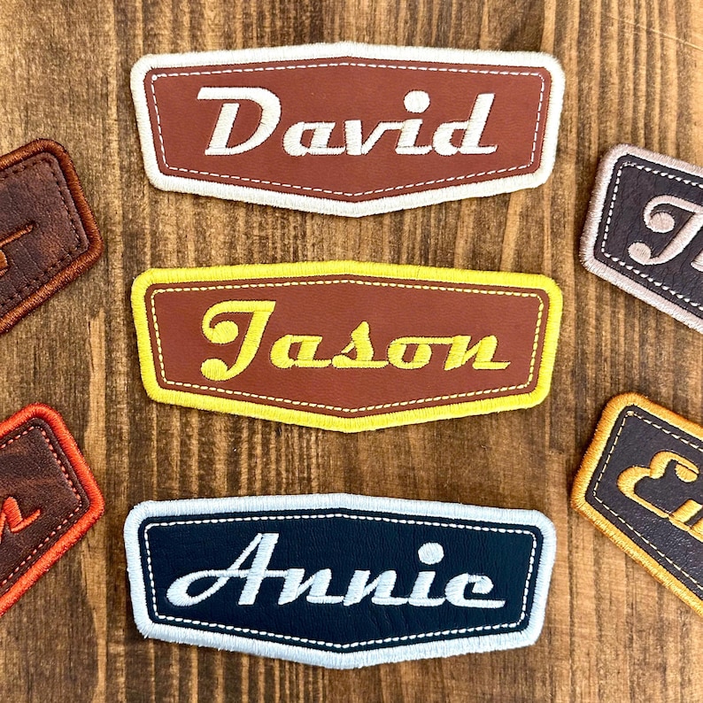 May include: Embroidered name patches in brown, yellow, and navy blue. The patches feature names like "David", "Jason", and "Annie" in white or yellow script. Each patch has a contrasting border and is set against a wooden background.