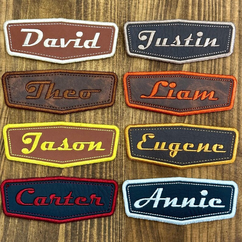 May include: A collection of personalized name patches in various colors. Each patch features a name embroidered in a contrasting color, such as "David" in white on a brown patch, and "Annie" in white on a navy patch. The patches have a stitched border.