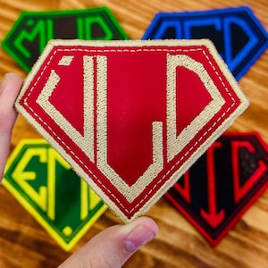 May include: A collection of embroidered patches in a diamond shape. The patches feature various color combinations, including red with gold stitching, green with white, and black with red. Each patch displays unique letter combinations.