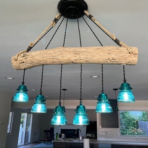 May include: A rustic chandelier with six teal blue glass shades hanging from a natural wood branch. The branch is suspended from the ceiling with rope and black wire.