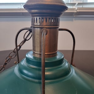 May include: A green metal lampshade with a brass top and a chain hanging from it. The lampshade has a rounded shape and a smooth surface.