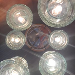 May include: A unique ceiling light fixture composed of multiple clear glass shades with decorative edges, each housing a lit bulb. The fixture is mounted on a dark surface, with a decorative plate in the center.