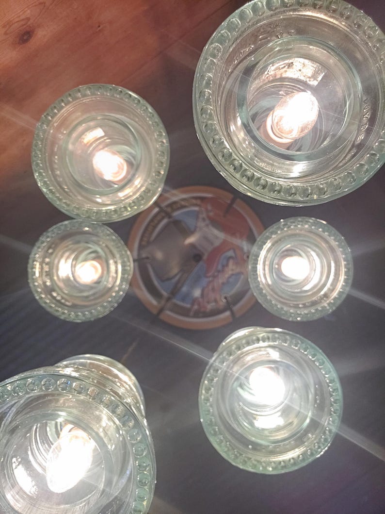 May include: A distinctive ceiling light fitting featuring several clear glass shades with patterned rims, each containing a lit bulb. The fitting is mounted on a dark surface, with a decorative plate at the centre.